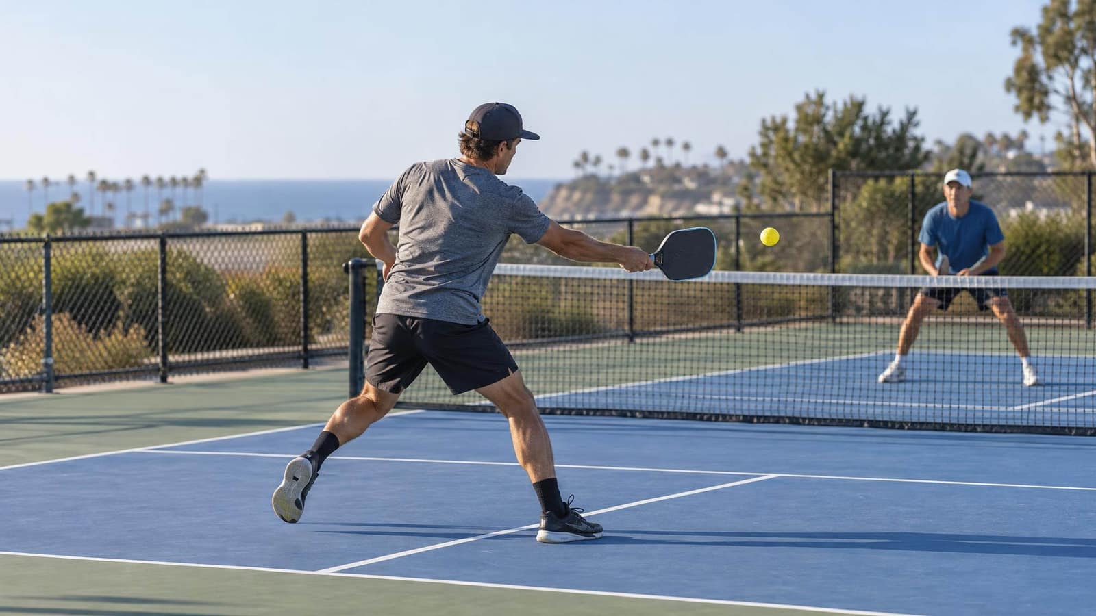 Two people playing singles pickleball on an outdoor court above the coast