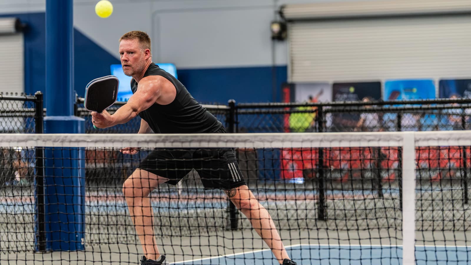 A player hitting a pickleball at the net on an indoor court